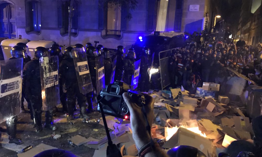 Agents de policia davant d'una foguera que comença a cremar a l'entorn de la delegació del govern espanyol a Barcelona el 15 d'octubre del 2019. Pla general. (Horitzontal)