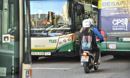 Una moto passejant per un carrer de Sabadell entre dos autobusos