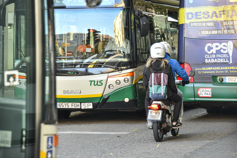 Una moto passejant per un carrer de Sabadell entre dos autobusos